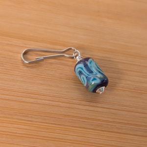 May include: A silver key chain with a blue and white glass bead. The bead has a swirling pattern.