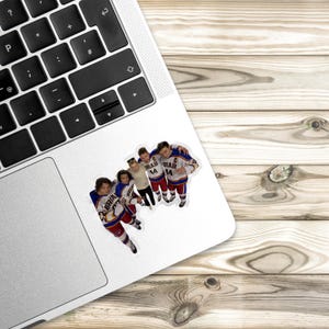 May include: A die-cut sticker featuring four hockey players in white, blue, and red jerseys with the text BRIAR and the number 44 visible on the front. The sticker is applied to the silver palm rest area of a laptop with a black keyboard.