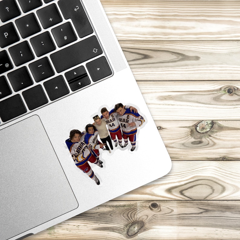 May include: A die-cut sticker featuring four hockey players in white, blue, and red jerseys with the text BRIAR and the number 44 visible on the front. The sticker is applied to the silver palm rest area of a laptop with a black keyboard.