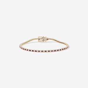 Könnte beinhalten: Ein goldenes Armband mit einer Reihe kleiner, roter Edelsteine. Das Armband hat einen sicheren Verschluss. Die Edelsteine sind gleichmäßig über die Länge des Armbands verteilt.
