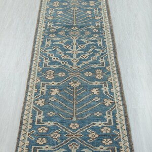 Könnte beinhalten: Ein rechteckiger, blauer Läuferteppich mit einem detaillierten, symmetrischen Muster. Das Design zeigt stilisierte Blumen- und geometrische Formen in Beige- und Brauntönen. Der Teppich hat einen braunen Rand und einen Fransenrand. Ca. 200 cm lang.