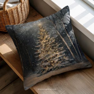 May include: Square cushion with a winter forest scene, featuring a glowing Christmas tree. The artwork uses shades of grey, black, and brown, with golden lights on the tree. The cushion is placed on a wooden surface.