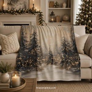 Könnte beinhalten: Eine weiche Wohndecke mit einer winterlichen Waldszene, dunklen Tannenbäumen, einem hellbeigen Hintergrund und verstreuten warmweißen Lichterketten, die einen leuchtenden Effekt auf dem Stoff erzeugen, drapiert über einem neutralen Sofa.