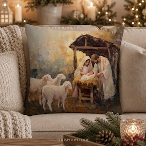 May include: A square throw pillow featuring an impressionistic painting of a nativity scene. The artwork depicts a figure in a white head covering and a figure in a white robe standing over a baby in a manger, surrounded by three white sheep.