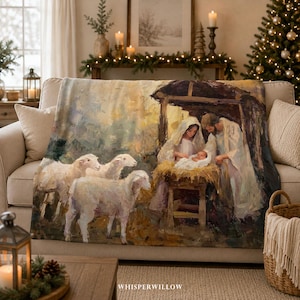 Pode incluir: Uma manta macia com uma cena de natividade impressa, apresentando uma manjedoura central, figuras de dois adultos e três ovelhas em primeiro plano. A arte utiliza um estilo pictórico com tons quentes e suaves de dourado, castanho e creme.