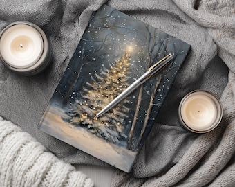 May include: A rectangular notebook featuring a winter forest scene with a glowing, illuminated Christmas tree at its center. A silver ballpoint pen rests diagonally across the cover. The text WhisperWillow is printed at the bottom.