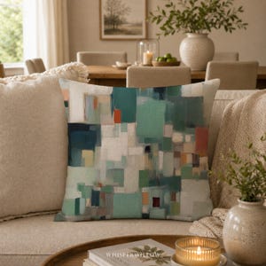 May include: A square throw pillow featuring an abstract geometric pattern of overlapping rectangles and squares in shades of teal, sage green, white, and burnt orange. The design has a textured appearance with visible brushstroke effects.
