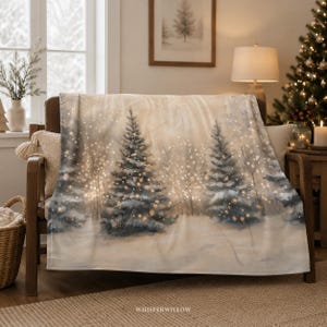 Könnte beinhalten: Eine weiche Wohndecke mit einem aufgedruckten Winterszenario, das schneebedeckte Tannen, leuchtende goldene Lichter und eine verschneite Landschaft zeigt. Unten mittig ist der Schriftzug WhisperWillow in weißer Schrift zu sehen.