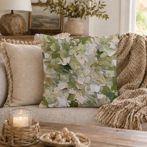 May include: A square throw pillow featuring an abstract oil painting design with thick, visible brushstrokes in various shades of sage green, olive, cream, and white. The textured pattern covers the entire front surface of the pillow.