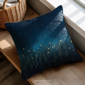 May include: Square decorative pillow with a dark blue night sky design. The pillow features a painted scene of tall grass with glowing yellow lights, and a starry sky. The text "WHISPERWILLOW" is at the bottom.