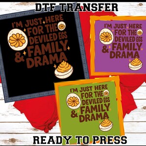 May include: DTF transfer designs featuring the text "I'M JUST HERE FOR THE DEVILED EGS & FAMILY DRAMA" with deviled egg graphics. The designs are in black, purple, and green frames, with the words "READY TO PRESS" at the bottom.