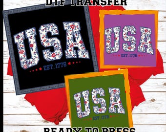 May include: Three DTF transfer designs featuring the word "USA" in a floral pattern, with "EST. 1776" below. The designs are on black, purple, and green backgrounds, with the text "DTF TRANSFER" and "READY TO PRESS".