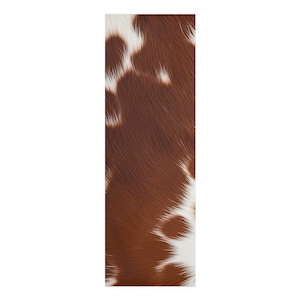 Pode incluir: Um tapete retangular com um padrão de pele de vaca. O tapete apresenta uma mistura de manchas marrons e brancas, criando uma estética natural e rústica. A textura do tapete parece macia e convidativa.