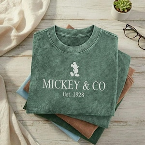 May include: A white ceramic mug with a black handle and the text "But First, Coffee" in a handwritten style. The mug is on a white surface. The mug is approximately 4 inches tall.