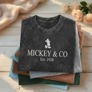 May include: A white ceramic mug with a black handle and the text "But First, Coffee" in a bold, black font. The mug is sitting on a wooden surface. The mug is approximately 4 inches tall.