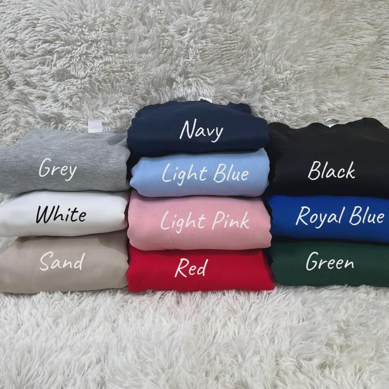 May include: A collection of folded sweatshirts in various colors, including grey, navy, light blue, black, white, light pink, royal blue, sand, red, and green. Each sweatshirt has its color name printed on it in white.