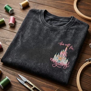 Puede incluir: Camiseta gris oscuro con cuello redondo y un dise&ntilde;o de castillo bordado en rosa, azul y dorado, con el texto "this will fix everything!". Se ven suministros de costura, como hilo y tijeras.