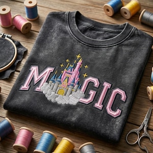 May include: A dark gray sweatshirt with the word "MAGIC" embroidered in pink, featuring a castle design. The sweatshirt is surrounded by spools of thread in various colors, embroidery hoops, and scissors, suggesting a craft theme.