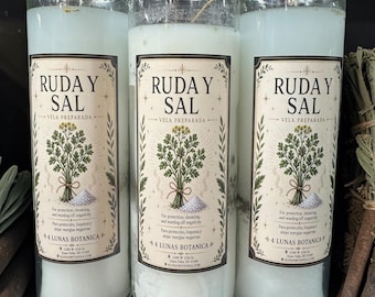 May include: Three tall, cylindrical glass candles filled with opaque white wax. Each features a cream-colored label with the text RUDAY SAL, VELA PREPARADA, and 4 LUNAS BOTANICA, alongside an illustration of a green herb bundle and a pile of salt.