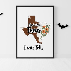 Pu&ograve; includere: Una stampa incorniciata con il contorno del Texas in un motivo a pelle di mucca. Il testo "She's from Texas, I can tell," &egrave; visualizzato. Fiori arancioni e foglie verdi sono sul lato destro del contorno del Texas. Due sagome di pipistrelli neri sono sul muro.