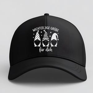 May include: Black baseball cap featuring a white graphic of three gnomes with different hat patterns and the text "Wicht(el)ige Gr&uuml;&szlig;e f&uuml;r dich". The cap has a curved brim and a button on top.