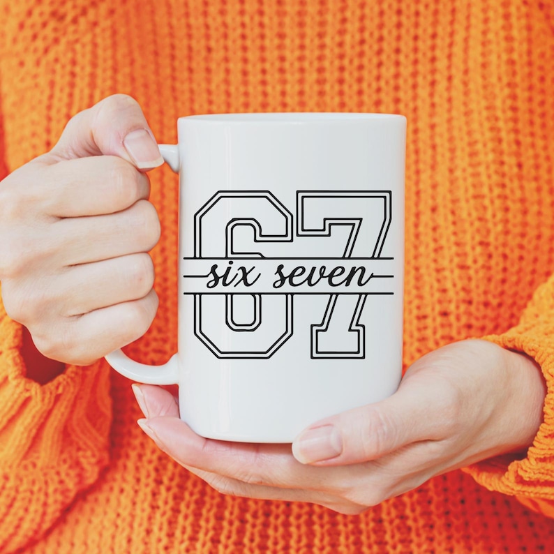 May include: White ceramic mug with the text "67 six seven" in a black outlined font. The mug is held by a person wearing an orange sweater. The mug is a standard size for coffee or tea.