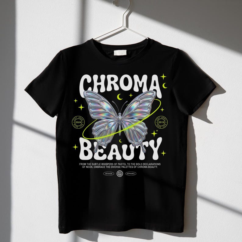 May include: A black t-shirt featuring a central iridescent butterfly graphic surrounded by a yellow orbital ring, small stars, and crescents. The text reads CHROMA BEAUTY, with smaller text below and circular emblems on each side of the butterfly.