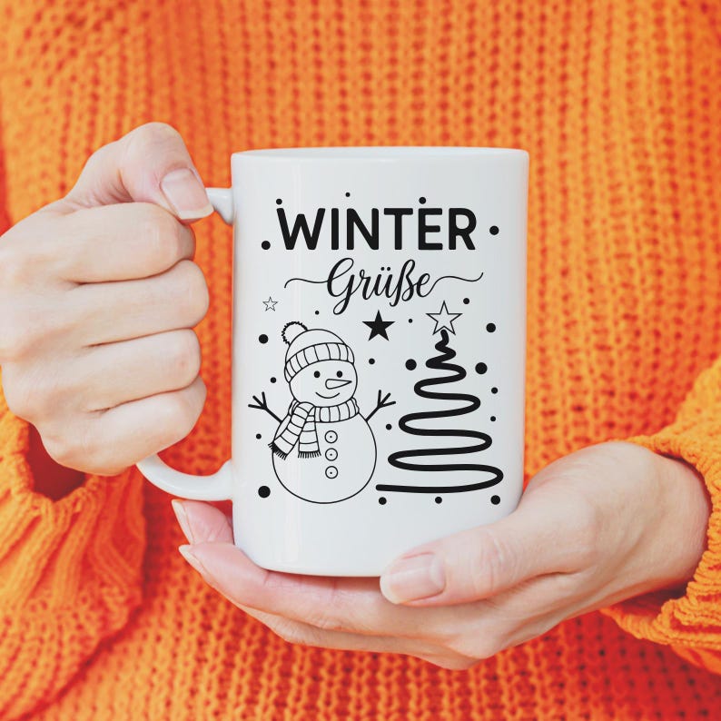 May include: White ceramic mug featuring a snowman design with a hat, scarf, and a Christmas tree. The mug has the words "Winter Gr&uuml;&szlig;e" in black script. The mug is held by a person wearing an orange sweater.