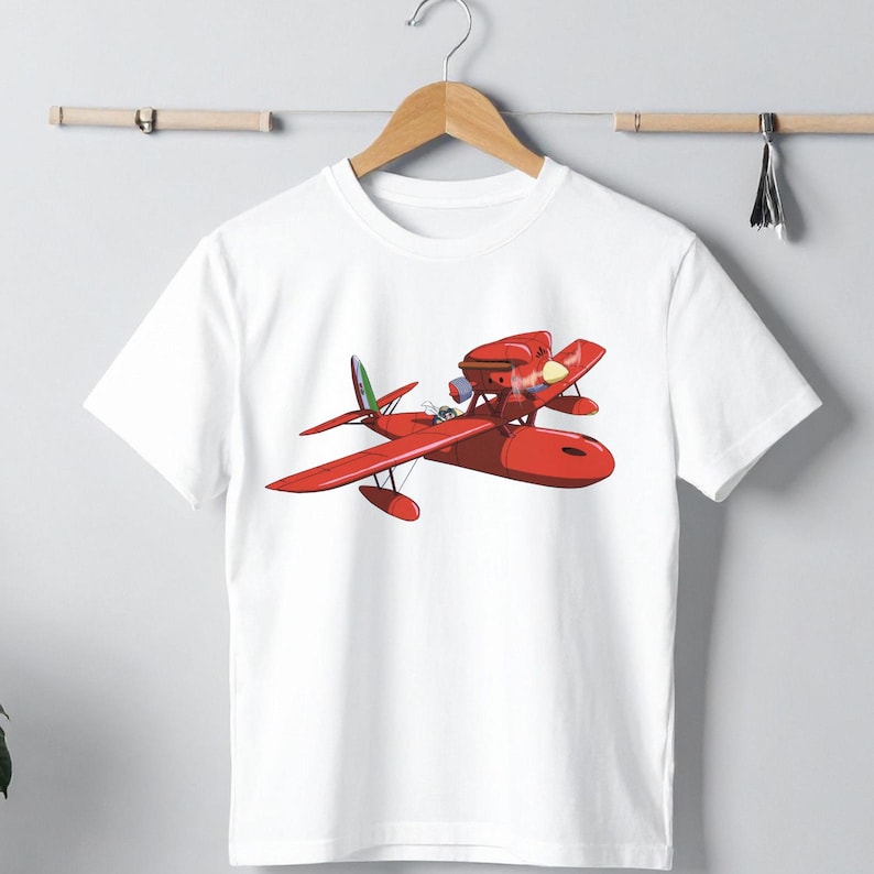 May include: White t-shirt featuring a vibrant red seaplane design. The illustration shows a detailed view of the aircraft, including its wings, pontoons, and cockpit. The seaplane has a green, white, and red tail fin. The design is centered on the shirt.