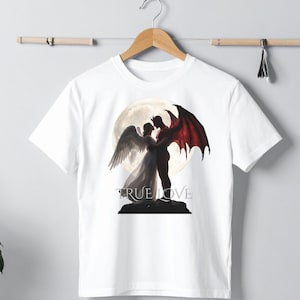 May include: A white short-sleeve t-shirt featuring a graphic print of an angel with white wings and a devil with red wings embracing in front of a large full moon. The text TRUE LOVE is printed in a serif font below the figures on a dark base.