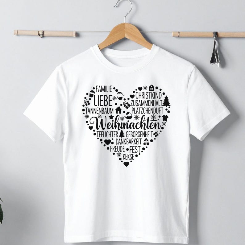 May include: White t-shirt with a heart-shaped design filled with German words and Christmas-themed icons. The words include "Liebe", "Weihnachten", and "Familie". The design is in black.