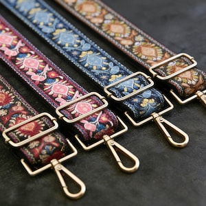 Può includere: Quattro tracolle colorate con finiture in metallo dorato. I cinturini presentano intricati disegni floreali nei toni del rosso, rosa, blu e marrone. Ogni cinturino ha una fibbia rettangolare e un moschettone girevole.