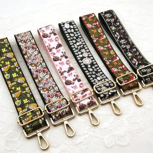 Könnte beinhalten: Sechs farbenfrohe, gemusterte Taschenriemen mit goldfarbener Hardware. Die Riemen weisen florale Designs in verschiedenen Farben auf, darunter Grün, Rosa und Schwarz. Jeder Riemen hat eine rechteckige Schnalle und einen Drehverschluss.