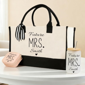 May include: A cream tote bag, small pink case, and glass tumbler with the text "Future MRS. Smith" in black. The tote bag has black handles and base. The tumbler has a bamboo lid and a straw. The small case is square.