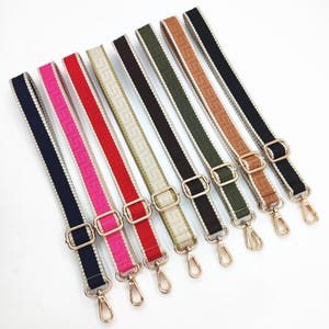 Peut inclure: Huit bandoulières de sac colorées. Chaque sangle présente une couleur différente, notamment le bleu marine, le rose, le rouge, le beige, le noir et le marron. Les sangles ont une boucle et des mousquetons dorés et un motif répété.
