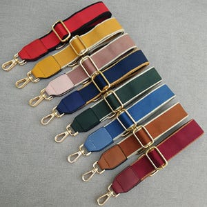 Può includere: Una selezione di tracolle colorate per borse, in varie tonalità tra cui rosso, giallo, rosa, blu navy, verde, blu, marrone e bordeaux. Ogni cinturino presenta elementi metallici dorati, tra cui fibbie regolabili e moschettoni girevoli.