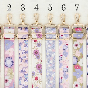 May include: Eight floral patterned bag straps with gold-colored metal hardware. The straps feature various designs with flowers in shades of pink, purple, and white. Each strap has a different floral pattern, offering a variety of styles.