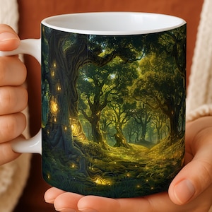 May include: White ceramic mug featuring a detailed forest scene with glowing lights. The artwork depicts a lush, green forest with tall trees and a path leading into the distance. The mug is held by a person wearing a cream-colored sweater.