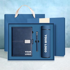 May include: A blue gift set containing a notebook, pen, and insulated flask. The notebook has a silver clasp and the text "YOUR LOGO". The flask and notebook have the text "YOUR LOGO". The set is presented in a blue gift box with a matching gift bag.