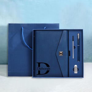 May include: A blue gift set featuring a personalized journal with the name "Deborah" and a matching pen and pencil set. The set is presented in a gift box and includes a matching gift bag.