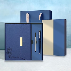 May include: A blue gift set featuring a notebook, pen, and refill, presented in a matching box. The notebook has a floral design and the name "Melissa Efe" printed on it. The set includes a gift bag with wooden handles.