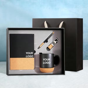 Può includere: Un set regalo nero con un taccuino, una penna, un apribottiglie e una tazza. Il taccuino e la tazza hanno una base in sughero e la scritta "YOUR LOGO". Il set è in una scatola nera con un sacchetto regalo nero.