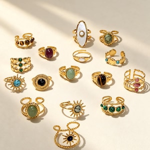 Peut inclure: Une collection de bagues ajustables dorées présentant diverses pierres précieuses et designs, incluant des motifs soleil, des cabochons ovales et des anneaux multi-pierres. Les bagues arborent des pierres variées comme la turquoise, l'œil-de-tigre, la malachite et la nacre.
