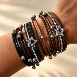 May include: A multi-strand wrap bracelet featuring black and brown leather-like cords, metallic silver-tone beads, and two silver-tone star charms. One section includes a row of clear rhinestones embedded in a black band, while another has a textured finish.