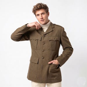 Puede incluir: Chaqueta verde oliva con cuatro bolsillos delanteros y cierre de botones. La chaqueta tiene un diseño clásico con solapas con muescas y charreteras. El modelo lleva un cuello alto crema debajo.