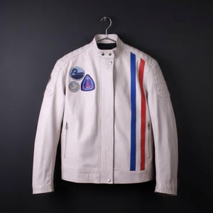May include: Cream-colored motorcycle jacket with a stand-up collar and a vertical red, white, and blue stripe. The jacket features several patches on the chest and left sleeve, and a zipper closure. The jacket is hanging on a metal hanger.