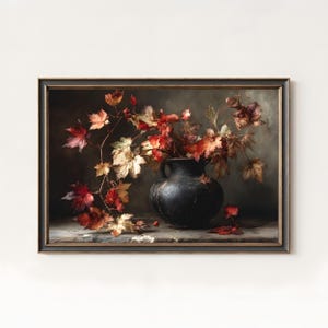 Puede incluir: Pintura enmarcada de naturaleza muerta con un jarrón negro lleno de hojas otoñales en tonos rojos, naranjas y amarillos. Las hojas se derraman sobre una superficie de madera. El fondo es de un color oscuro y apagado.
