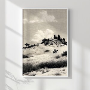 May include: Monochrome print of a rural landscape featuring a stone house atop a hill, with two figures on horseback in the foreground. The artwork is framed in a white border, with a cloudy sky above.