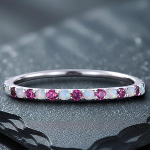 以下が含まれることがあります： ピンクと白の宝石が交互に並んだシルバーリング。細いバンドと丸い石の列が特徴で、繊細でエレガントなデザインです。宝石は互いに近くにセットされており、リング全体の輝きを高めています。