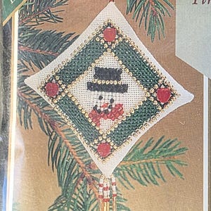 May include: A Mill Hill Tiny Treasured Diamonds cross stitch kit titled Friendly Frosty, MHTD10. The package features a diamond-shaped ornament with a snowman design, green border, red accents, and beaded fringe, including beads, treasures, and fabric.
